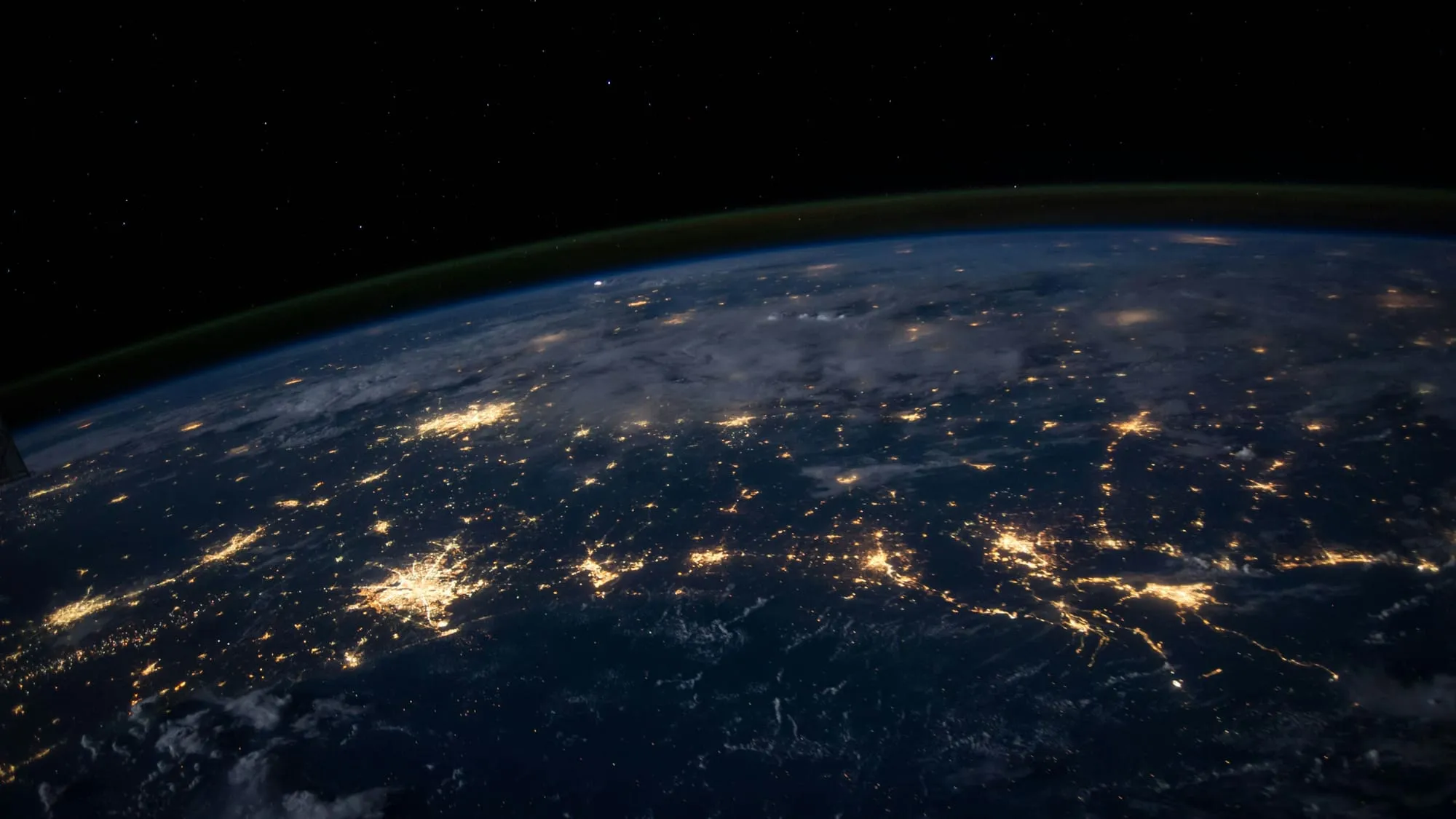 Earth at night seen from orbit, with clusters of city lights connected by thin lines of light under a dark sky